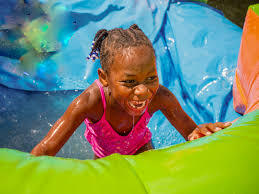 Smiling child sliding down a bright green water slide at a summer party in Cape Coral, FL.